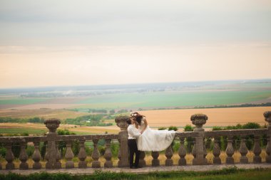 Güzel, romantik bir düğün. Yeni evliler. Eski kalenin yakınlarında sarılıyorlar.