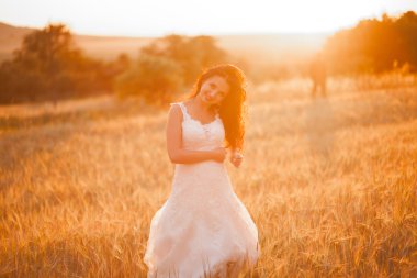 Mutlu, güzel, genç gelin gün batımında bir çayırda.