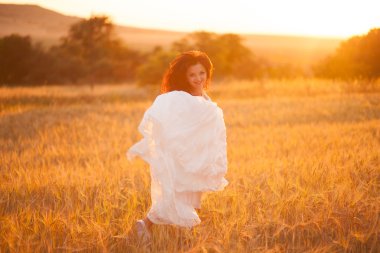 Mutlu, güzel, genç gelin gün batımında bir çayırda.