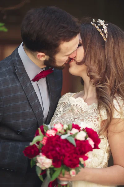 Couple de mariage étreignant, la mariée tenant un bouquet de fleurs dans sa main, marié embrassant — Photo