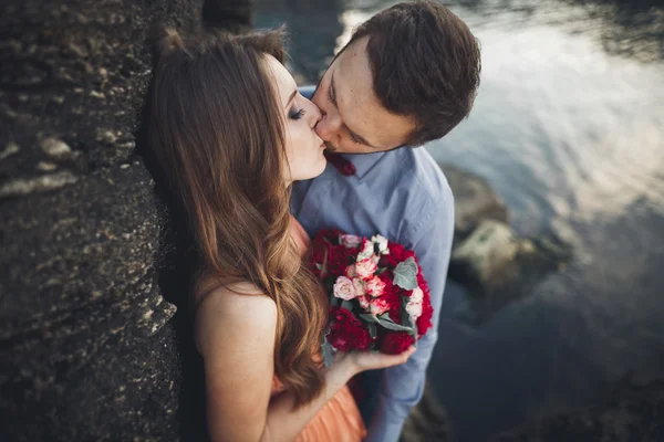 Boda pareja besándose y abrazándose en rocas cerca de mar azul — Foto de Stock