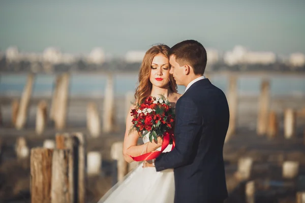 Pareja de boda, novio, novia con ramo posando cerca del mar al atardecer —  Fotos de Stock