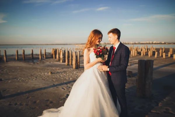 Brautpaar, Bräutigam, Braut mit Strauß posiert am Meer bei Sonnenuntergang — Stockfoto