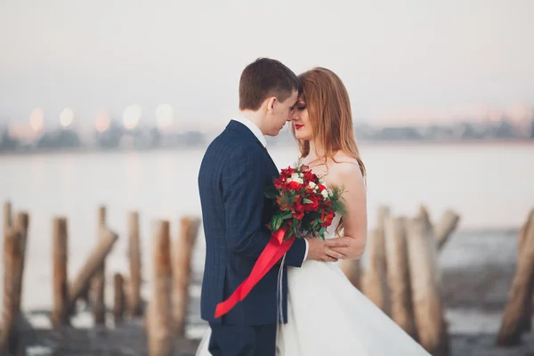 Svatební pár, ženich, nevěsta s kyticí pózuje u moře na západ slunce — Stock fotografie