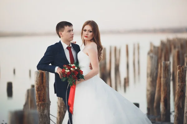 Όμορφο γάμο νεαρό ζευγάρι, νύφη και ο γαμπρός που παρουσιάζουν κοντά ξύλινων στύλων στη θάλασσα φόντο — Φωτογραφία Αρχείου