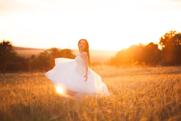 Happy beautiful young bride outside on a summer meadow at the sunset.