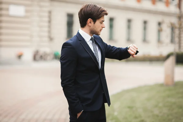 Homem de negócios confiante olhando em seu relógio de pulso em terno — Fotografia de Stock