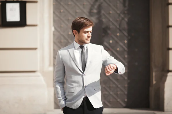 Homem de negócios confiante olhando em seu relógio de pulso em terno — Fotografia de Stock