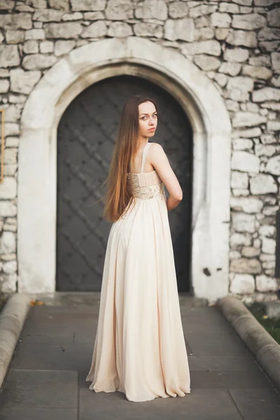 Jonge vrouw met lange jurk en haren poseren in park in de buurt van de oude poort — Stockfoto