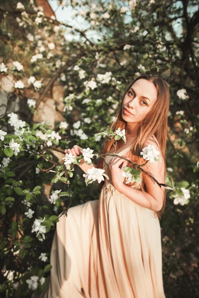 Junges schönes Mädchen in einem langen Kleid und einem Blumenkranz in der Nähe des Fliederstrauches — Stockfoto