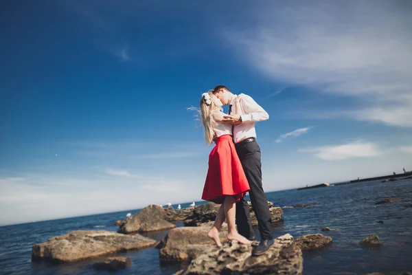 Romántica pareja amorosa posando sobre piedras cerca del mar, cielo azul — Foto de Stock