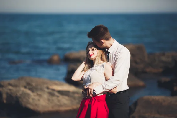 Romantica coppia amorevole posa su pietre vicino al mare, cielo blu — Foto Stock