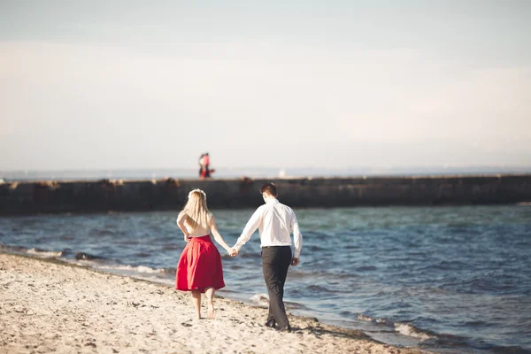 Νεαρό ζευγάρι χαρούμενος περπάτημα στην παραλία χαμογελώντας εκμετάλλευση γύρω από το άλλο. Ιστορία αγάπης — Φωτογραφία Αρχείου