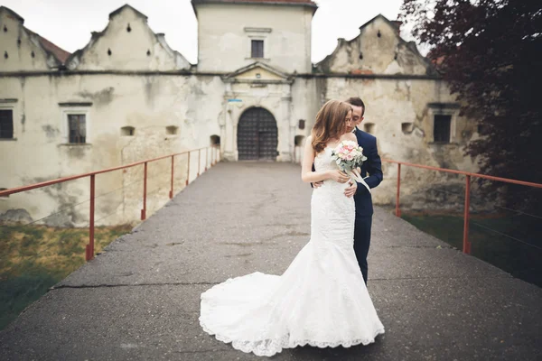 Щаслива весільна пара обіймає і посміхається один одному на фоні старого замку — стокове фото