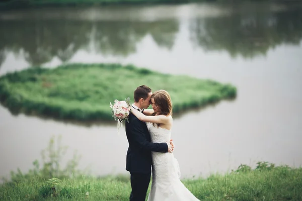 Красивая свадебная пара целуется и обнимается у озера с островом — стоковое фото