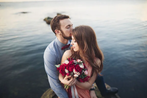 Pareja de boda sentada en piedra grande alrededor del mar azul —  Fotos de Stock