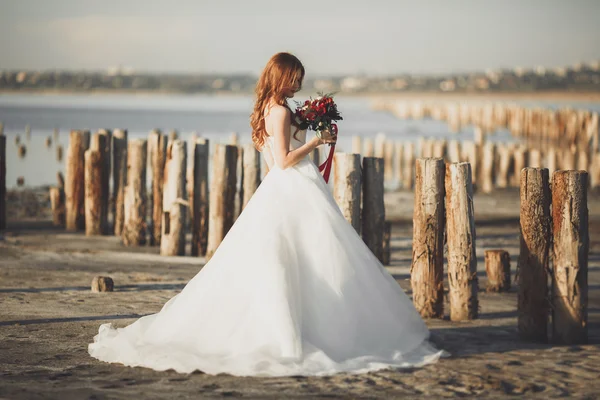 Mooie dame, bruid poseren in een trouwjurk in de buurt van zee bij zonsondergang — Stockfoto