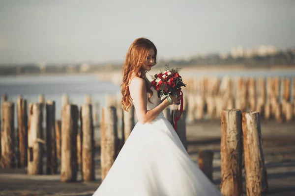 Romantic beautiful bride in white dress posing on the background sea and wooden poles — Stock Photo, Image