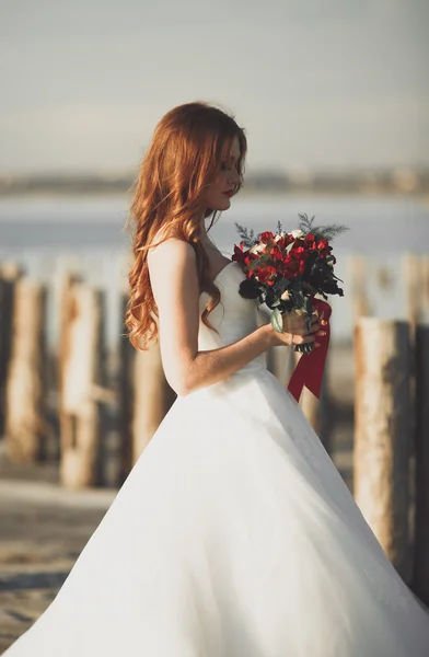 Hübsche Dame, Braut posiert in einem Brautkleid am Meer bei Sonnenuntergang — Stockfoto