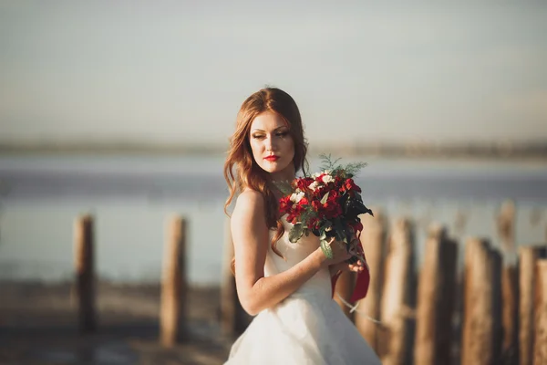 Romantic beautiful bride in white dress posing on the background sea and wooden poles — Stock Photo, Image