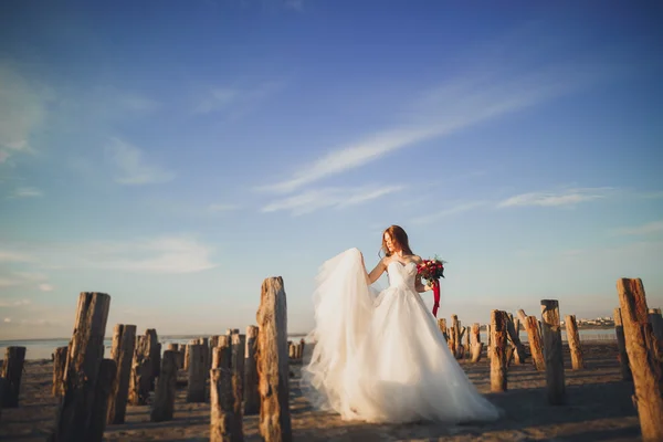 Jolie dame, mariée posant dans une robe de mariée près de la mer au coucher du soleil — Photo