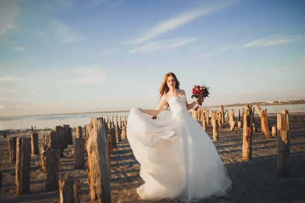 Bella dama, novia posando en un vestido de novia cerca del mar al atardecer —  Fotos de Stock