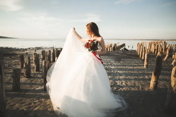 Bella giovane sposa con bouquet da sposa in posa sullo sfondo mare — Foto Stock