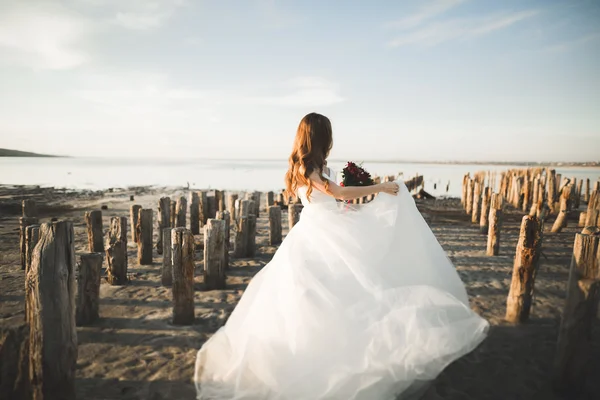 Bella signora, sposa in posa in un abito da sposa vicino al mare al tramonto — Foto Stock