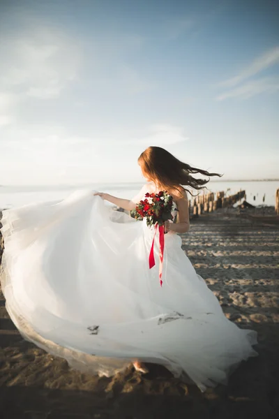 Ładna pani, panna młoda pozowanie w sukni ślubnej w pobliżu morza na zachód słońca — Zdjęcie stockowe