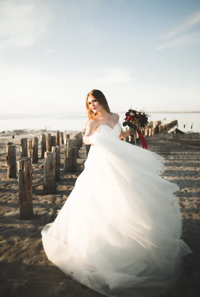 Romantica bella sposa in abito bianco in posa sullo sfondo mare e pali di legno — Foto Stock