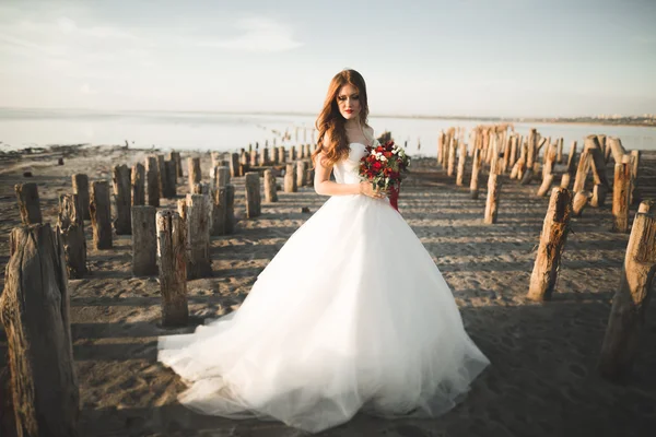 Bella signora, sposa in posa in un abito da sposa vicino al mare al tramonto — Foto Stock