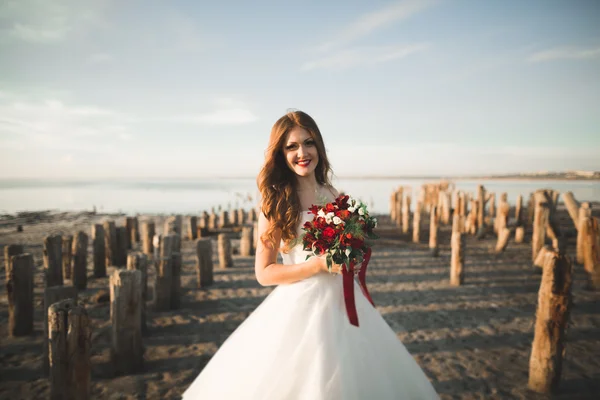 Bella giovane sposa con bouquet da sposa in posa sullo sfondo mare — Foto Stock