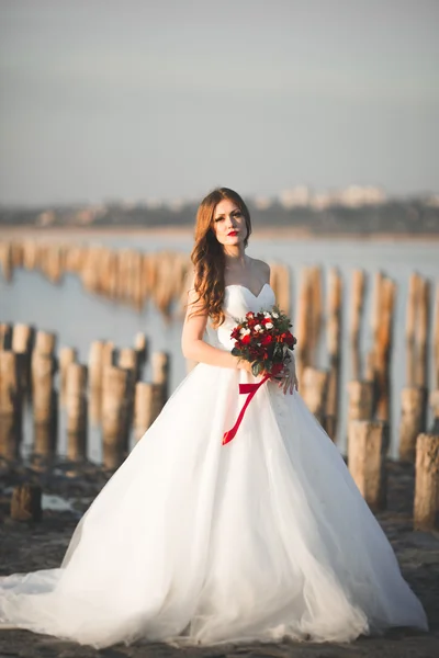 Bella signora, sposa in posa in un abito da sposa vicino al mare al tramonto — Foto Stock