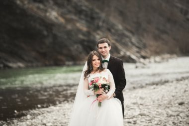 Öpüşme ve taşlarla Nehri yakınında kucaklayan güzel düğün çifti