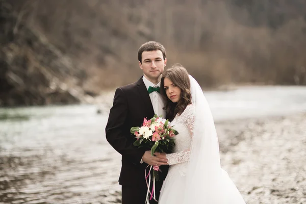 Красива весільна пара цілується і обіймається біля річки з камінням — стокове фото