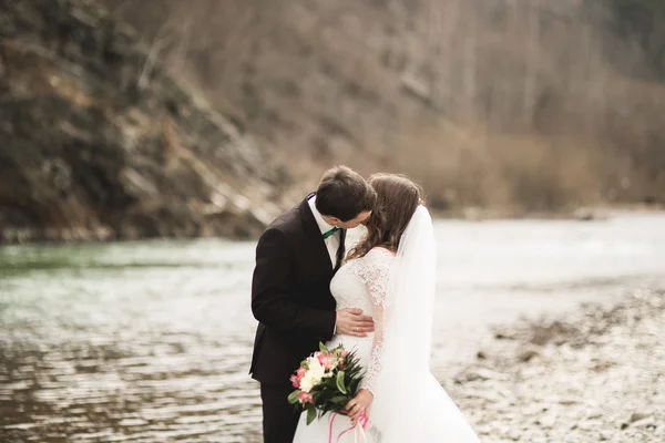 Schönes Hochzeitspaar küsst und umarmt sich in Flussnähe mit Steinen — Stockfoto
