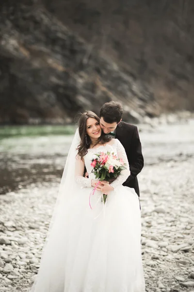 Gyönyörű esküvői pár csók, és átfogó, kövekkel-folyó közelében — Stock Fotó