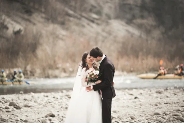 Beautifull wedding couple kissing and embracing near river with stones — Stock Photo, Image