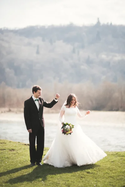 Bella coppia di nozze, sposa, sposo in posa e camminare in campo sullo sfondo di alte montagne — Foto Stock