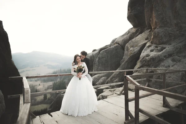 Happy bröllopsparet, bruden och brudgummen poserar nära klipporna med vacker utsikt — Stockfoto