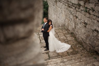Güzel, romantik bir düğün. Yeni evliler. Eski kalenin yakınlarında sarılıyorlar.