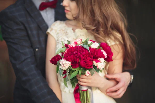 Γαμήλιο ζευγάρι αγκαλιάζει, κρατώντας ένα μπουκέτο λουλούδια στο χέρι της νύφης, γαμπρού αγκαλιάζοντας — Φωτογραφία Αρχείου