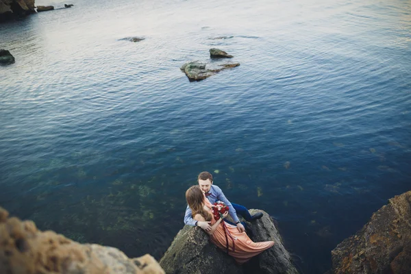 Pareja de boda sentada en piedra grande alrededor del mar azul — Foto de Stock