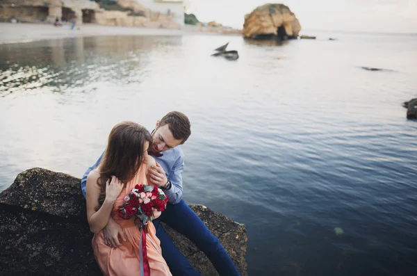 Pareja de boda sentada en piedra grande alrededor del mar azul — Foto de Stock