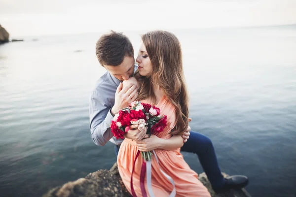 Boda pareja besándose y abrazándose en rocas cerca de mar azul —  Fotos de Stock