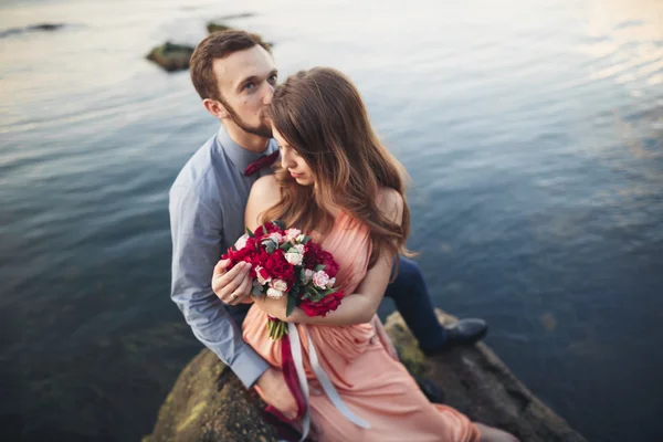 Pareja de boda sentada en piedra grande alrededor del mar azul — Foto de Stock