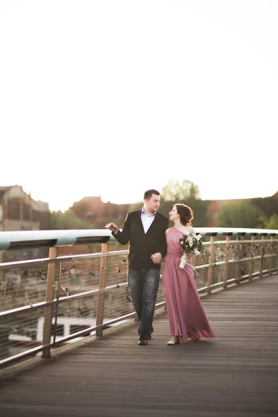 Casal de amor elegante, noivo, noiva com vestido rosa beijando e abraçando em uma ponte ao pôr do sol — Fotografia de Stock