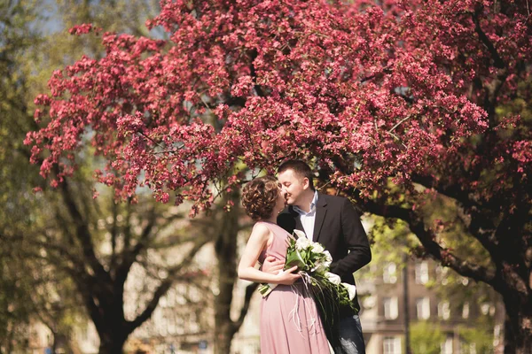 Unga bröllop par poserar nära träd med blommor — Stockfoto