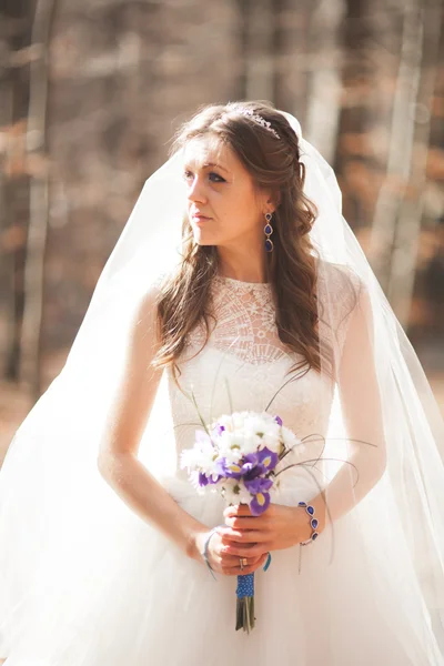 Wunderschöne Braut im eleganten Kleid mit Blumenstrauß und posiert in der Nähe des Waldes — Stockfoto