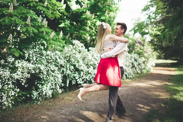 Jeune beau couple baisers et câlins près des arbres avec des fleurs dans le parc d'été — Photo